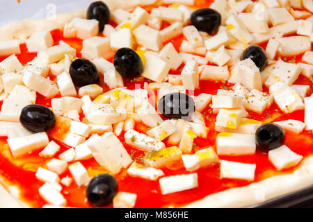 Raw pizza decorated mozzarella, black olives and tomato sauce ready to be baked Stock Photo