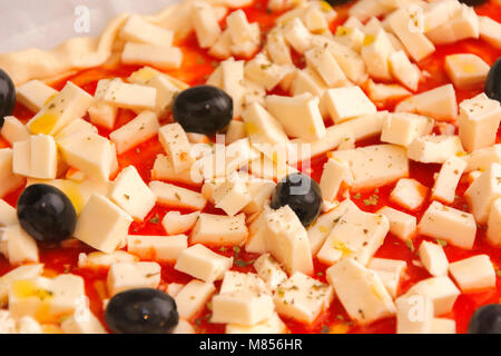 Raw pizza decorated mozzarella, black olives and tomato sauce ready to be baked Stock Photo