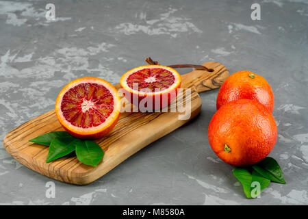 Sliced and whole ripe juicy Sicilian Blood oranges fruits over concrete texture background. Top view with space. Stock Photo