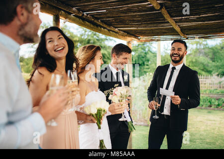 Best man giving speech to newlywed couple at wedding reception. Group of friends gathering for wedding reception. Stock Photo