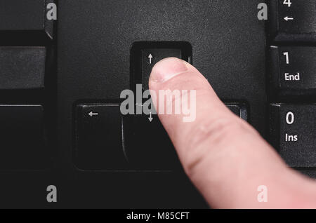 Human finger pressing the directional up key from a black keyboard. Stock Photo