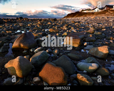 The rocky Llandanwg Beach is warmly lit as the sun sets over Tremadog Bay along the North Welsh Coast. Stock Photo