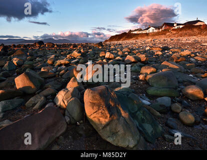 The rocky Llandanwg Beach is warmly lit as the sun sets over Tremadog Bay along the North Welsh Coast. Stock Photo