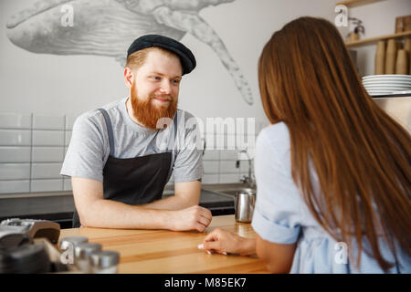 Coffee Business Concept - young beared handsome barista talking with beautiful caucasian customer in modern coffee shop. Stock Photo