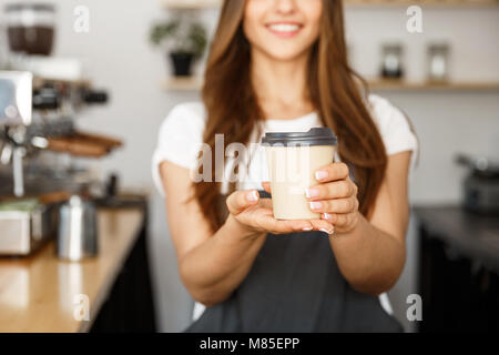 Coffee Business Concept - Beautiful Caucasian lady smiling at camera offers disposable take away hot coffee at the modern coffee shop Stock Photo