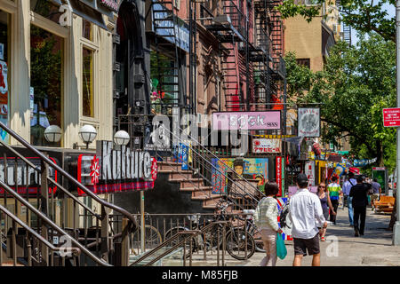 People walking past shops and buildings with cast iron fire escapes in St Marks Place In The East Village, Manhattan ,New York City Stock Photo