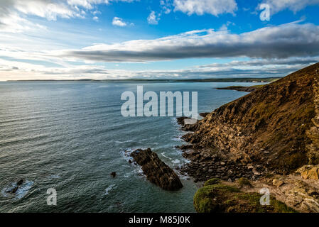 Scenic view of cliffs in  Old Head of Kinsale peninsula in Ireland with green hills at sunset. Stock Photo