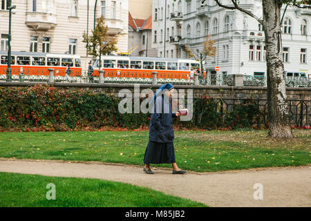 A nun with the Holy Bible in his hand is walking along the road down the street against the backdrop of the architecture of the city and the tram. Aut Stock Photo