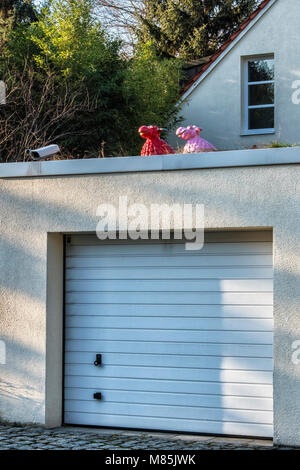 Berlin, Zehlenfdorf. House security system, CCTV camera and comical red and pink sheep ornament on garage roof of suburban home Stock Photo