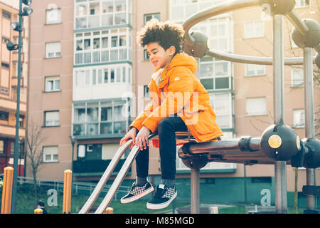 Happy kid in orange coat climbing on the playground in a sunny day Stock Photo