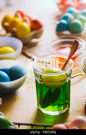 Dyeing eggs for Easter holidays, a green egg made with natural colorant inside a jar, with colored eggs around on a wooden background Stock Photo