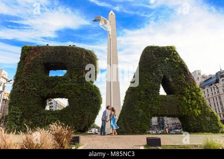 A couple of tourist kissing in front of the Obelisk monument on Avenida 9 de Julio. Buenos Aires, Argentina. Stock Photo