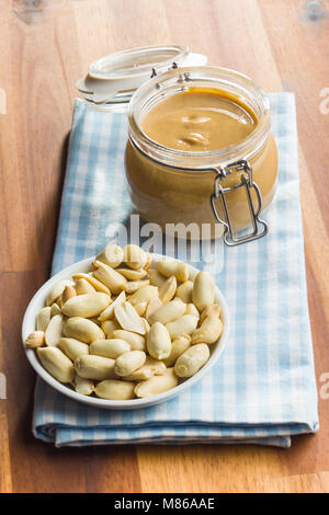 Peanut butter in jar and peanuts on wooden table. Stock Photo