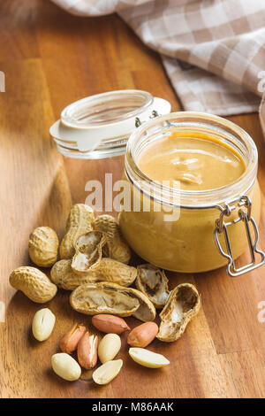 Peanut butter in jar and peanuts on wooden table. Stock Photo