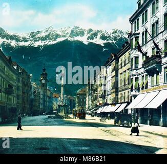 Colorized photo of a street scene on the Maria-Theresien-Strasse, Innsbruck, Austria, 1907. The St. Anne's Column and Spitalskirche (Hospital Church) are visible. (Photo by Burton Holmes) Stock Photo