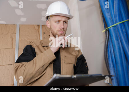young handsome builder thinking about something while holding clipboard Stock Photo