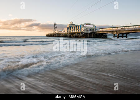 Rushing tide at the pier in Bournemouth, Dorset illuminated by the early morning winter sunrise