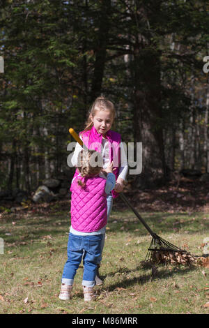 Two sisters helping rake leaves on a cool autumn day in Maine Stock Photo