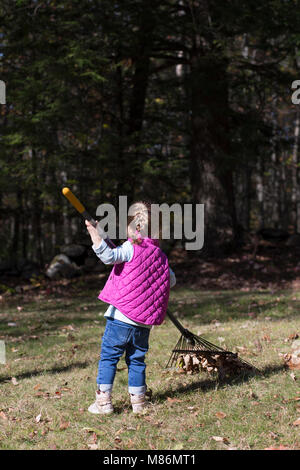 Toddler girl learning to rake leaves on a cool autumn day in Maine Stock Photo