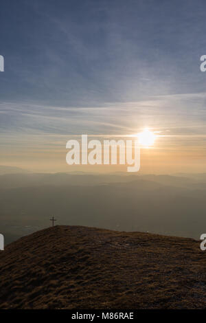 Cross on top of Mt. Serrasanta (Umbria, Italy), with warm golden hour colors and sun low on the horizon Stock Photo