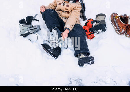 Boy sitting in the snow putting on his ice-skates Stock Photo