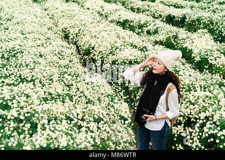 Young woman agronomist standing in a field of blooming chrysanthemum flowers. Looking into distance. Stock Photo