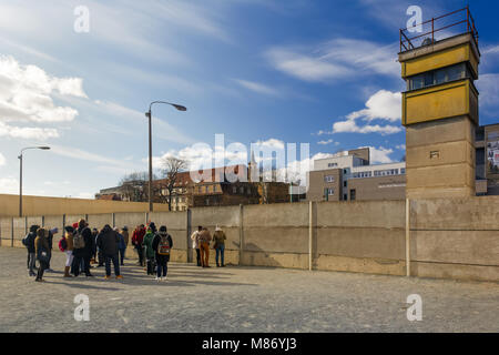 Group of tourists standing in front of the remains of Berlin Wall (Berliner mauer) Berlin, Germany. A former security tower is seen in the corner Stock Photo