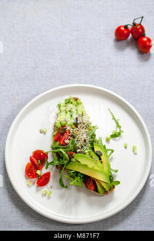 Rye toast with avocado, tomatoes and alfalfa sprouts Stock Photo