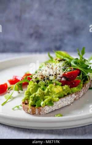 Rye toast with avocado, tomatoes and alfalfa sprouts Stock Photo