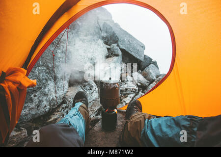 Man traveler cooking in pot on stove burner relaxing in camping tent Travel Lifestyle concept vacations outdoor mountains vacations Stock Photo