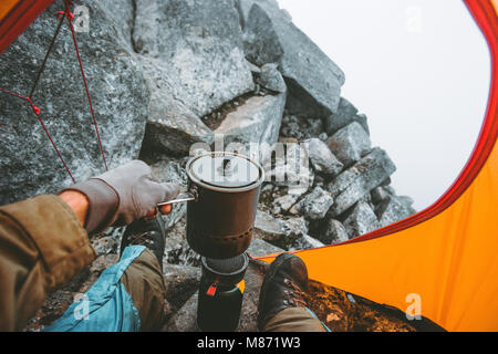 Man traveler cooking food in pot on stove burner in camping tent Travel Lifestyle concept vacations outdoor mountains vacations Stock Photo