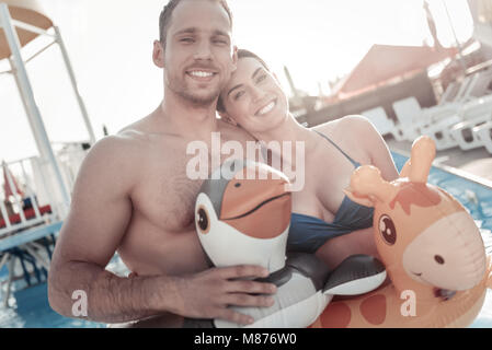 Relaxed young woman and man beaming while swimming in pool Stock Photo
