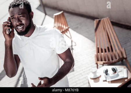 African american millennial guy at loss talking on smartphone Stock Photo