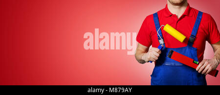 handyman with paint roller and level in hands on red background with copy space Stock Photo