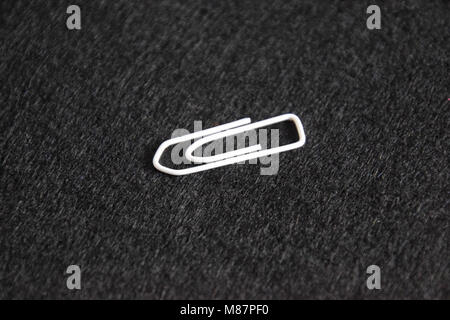 one white paperclip on black felt Background Stock Photo
