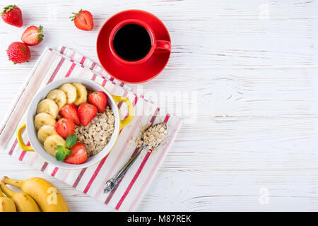 Breakfast oatmeal porridge with fruits berries and coffee cup. Oatmeal with strawberries and banana. Healthy breakfast concept. Top view Stock Photo