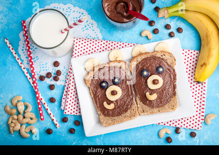 Kids breakfast with sandwiches and milk. Funny bear face sandwiches with chocolate paste, banana, nuts, and berries. Top view Stock Photo