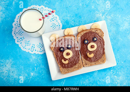Kids breakfast with sandwiches and milk. Funny bear face sandwiches with chocolate paste, banana, nuts, and berries. Top view Stock Photo