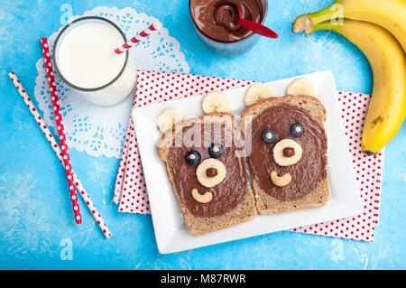 Children's breakfast with toasts and milk. Funny bear face sandwiches with chocolate paste, banana, nuts, and berries. Top view Stock Photo