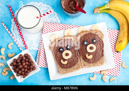 Children's breakfast with sandwiches and milk. Funny bear face sandwiches with chocolate paste, banana, nuts, and berries. Top view Stock Photo