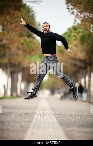 Excited Happy Man Jumping Up, Wearing Casual Clothes, in the park on day time Stock Photo