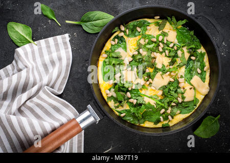 Omelet with eggs, spinach, pine nuts and vegetables. Spinach tortilla in pan on dark background.  Delicious breakfast or appetizer snack. Top view Stock Photo