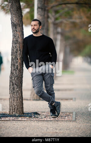 Confident Tough Handsome Man Posing, leaning against a tree, Shot with extreme Shallow Depth of Field Stock Photo