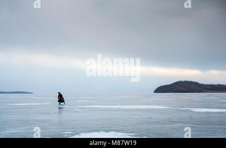 Hatgal, Mongolia, 4th March 2018: mongolian man dressed in traditional clothing skating on a frozen lake Khuvsgu Stock Photo