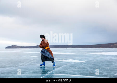 Hatgal, Mongolia, 4th March 2018: mongolian man dressed in traditional clothing skating on a frozen lake Khuvsgu Stock Photo