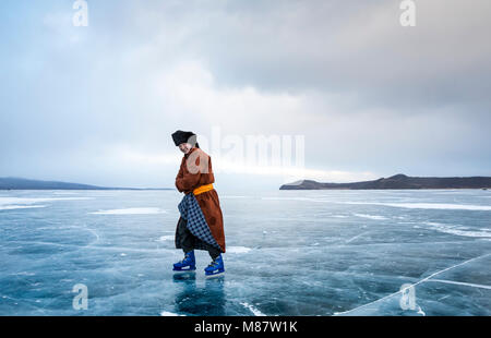 Hatgal, Mongolia, 4th March 2018: mongolian man dressed in traditional clothing skating on a frozen lake Khuvsgu Stock Photo