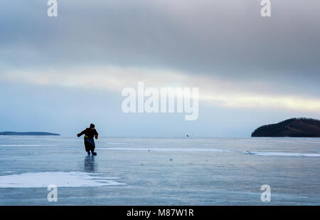 Hatgal, Mongolia, 4th March 2018: mongolian man dressed in traditional clothing skating on a frozen lake Khuvsgu Stock Photo