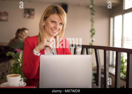 Business woman is working on laptop and drinking cup of coffee and glass of water in coffee shop, restaurant. Charming happy woman student using lapto Stock Photo