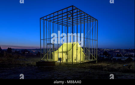 14 March 2018, Germany, Pforzheim: The art project 'The threatened house' (German: 'Das bedrohte Haus') pictured painted in yellow, lit and amidst high cage bars. The small, empty one-room house was turned into an art installation by artist and engineer Andreas Sarow. According to Sarow himself, his aim with this project is to call attention on 'the new things that are coming and what we must give up in exchange'. He also criticizes bourgeois construction design. Photo: Uli Deck/dpa Stock Photo