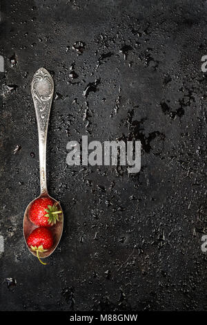 in a spoon a wet strawberry on a dark background with splashes of water, top view. Stock Photo